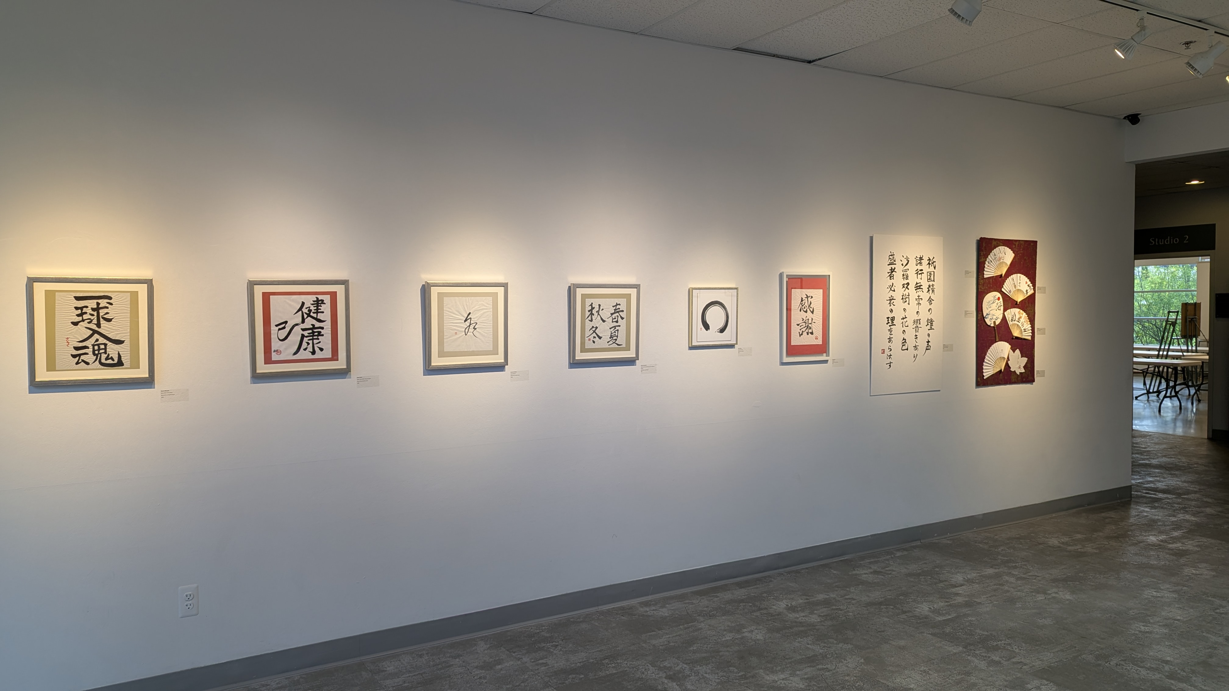 The Commons Gallery wall hung with framed shodo and ink works, the tall Heike Monogatari scroll near the right