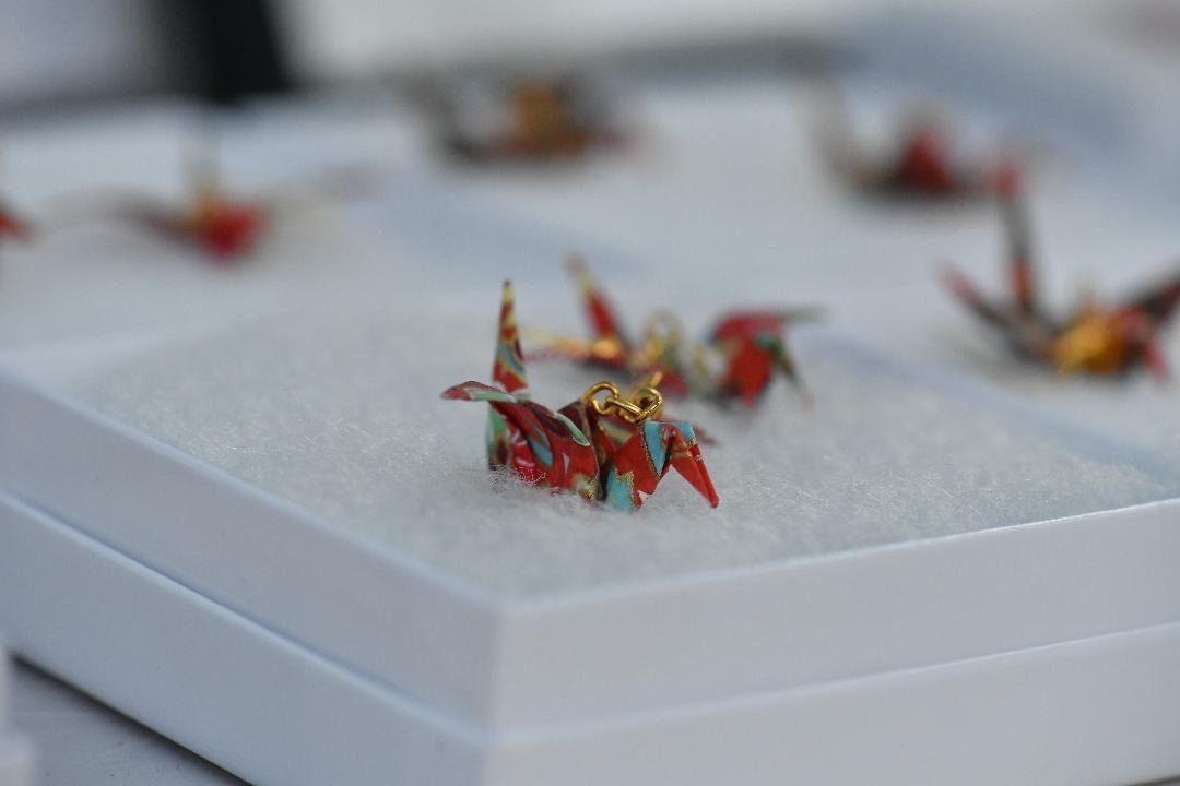 Close-up of red and gold origami crane earrings on a white jewelry box