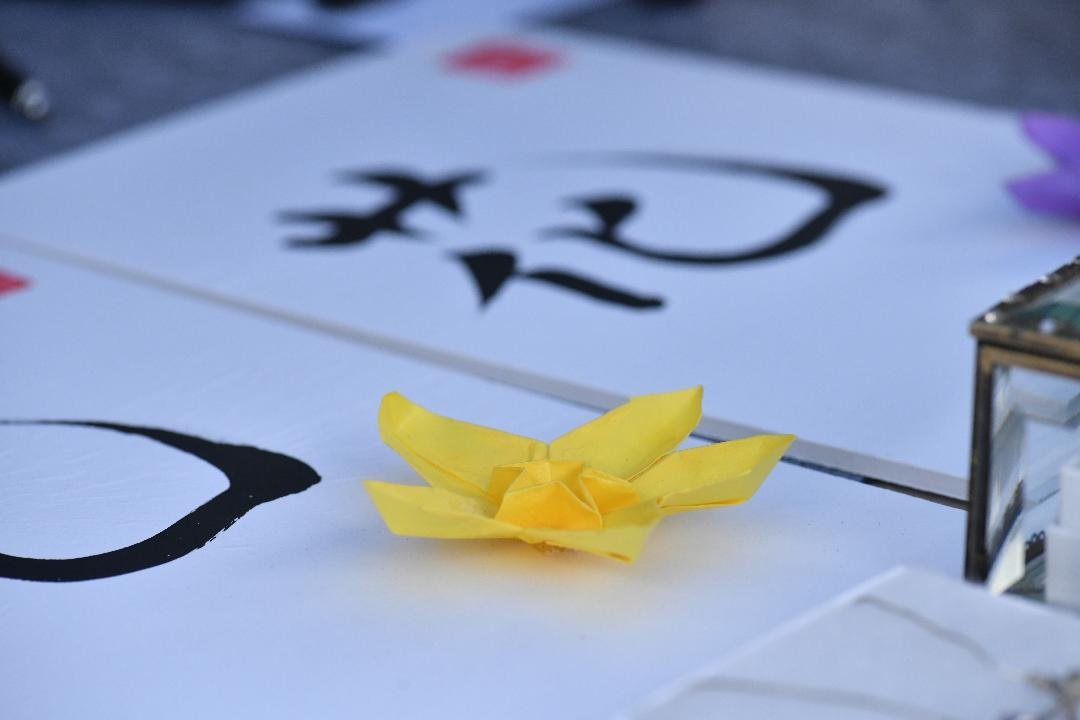 A yellow origami lily resting on the 花 calligraphy print