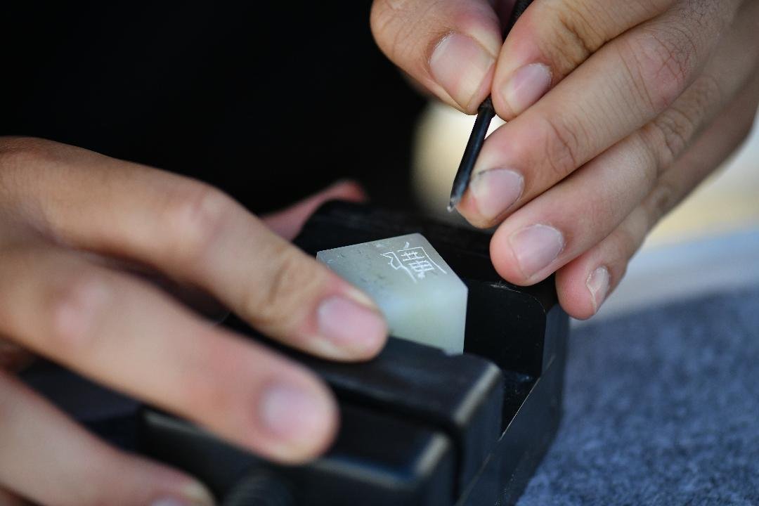 Hands carving a hanko name seal in a stone held in a carving vise