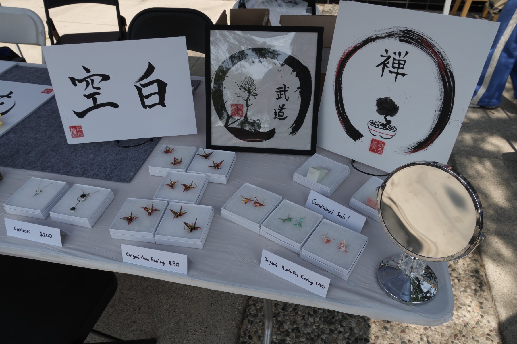 空白, 武道 and 禅 ensō works behind origami crane and butterfly earrings and a commissioned-seals sign