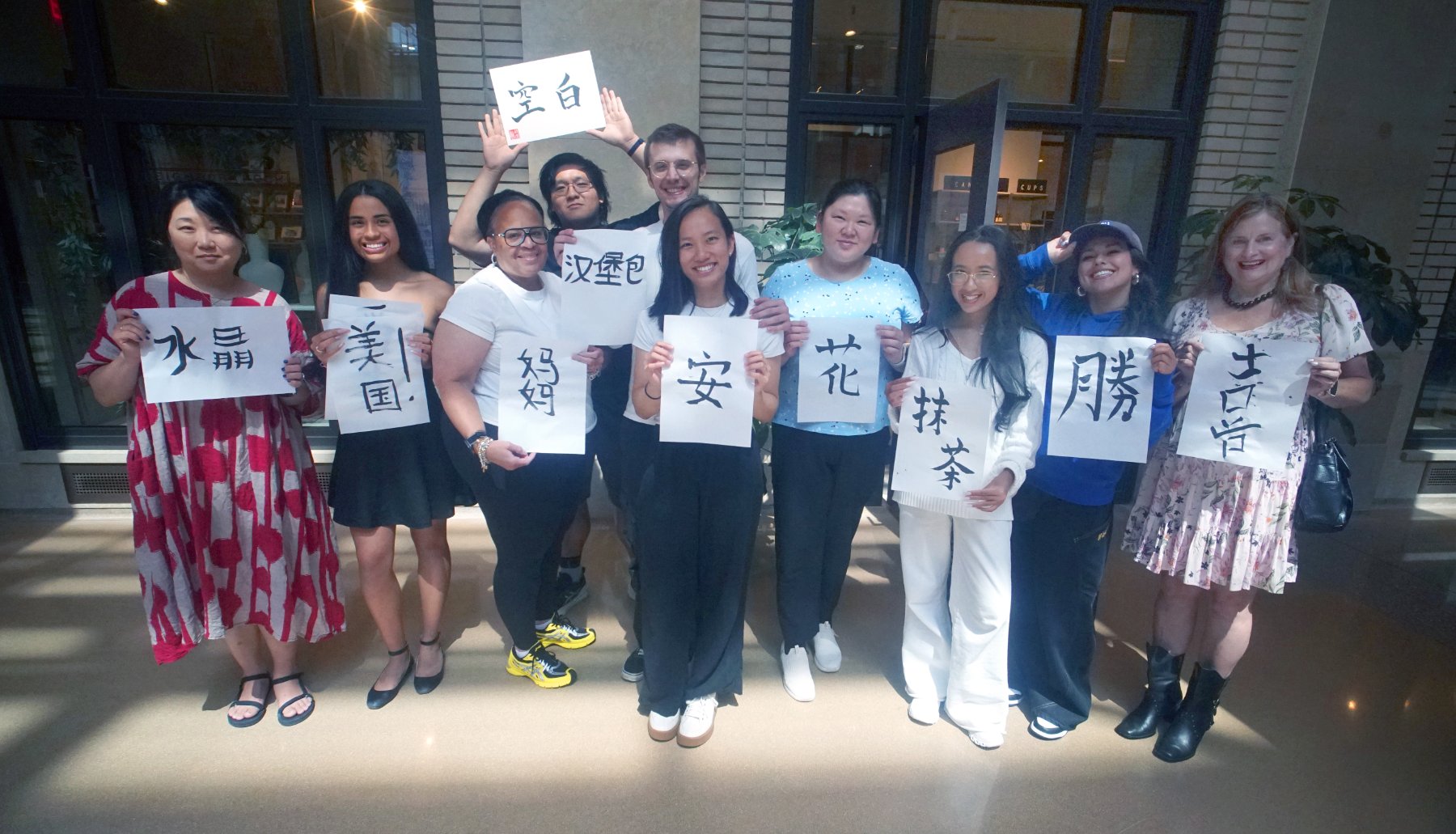 Students smiling with their brushed characters (水晶, 美国, 妈妈, 安, 花, 抹茶, 勝, 吉), with 空白 held overhead