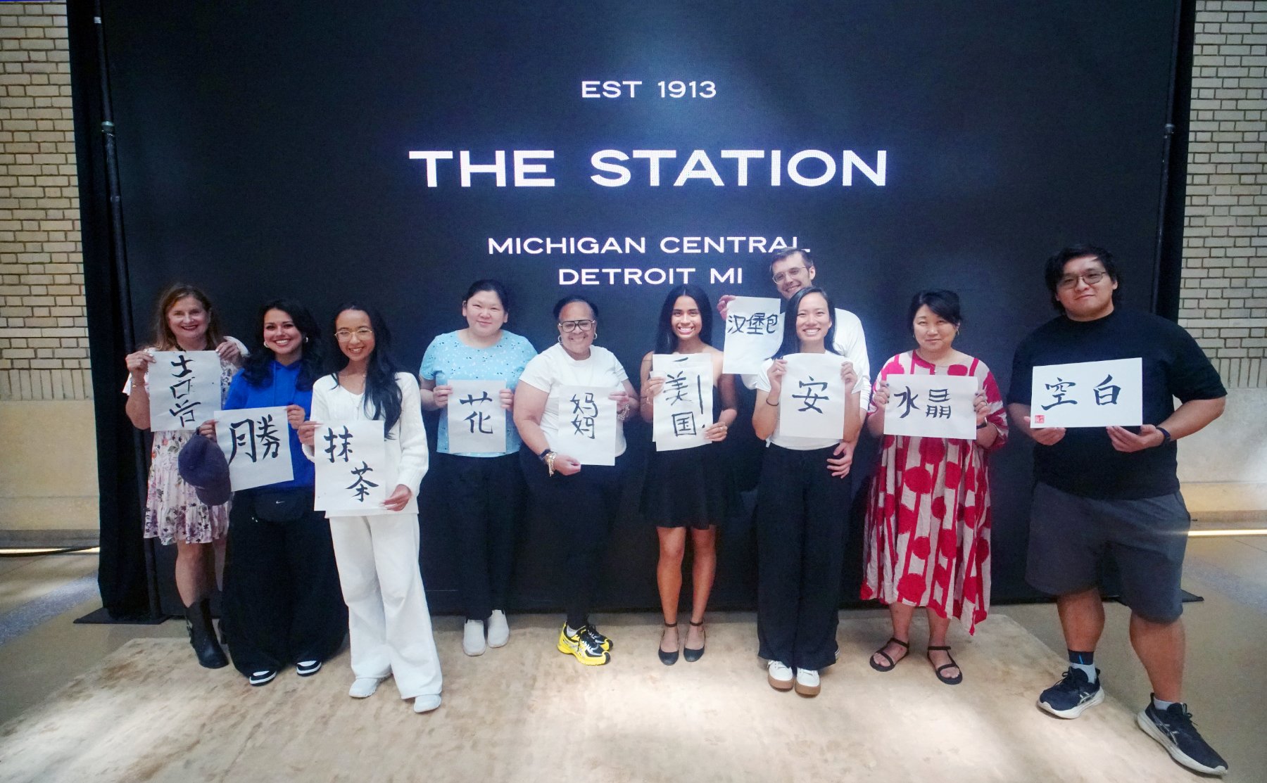 The class holding up their finished calligraphy in front of the Station sign: Est 1913, Michigan Central, Detroit MI