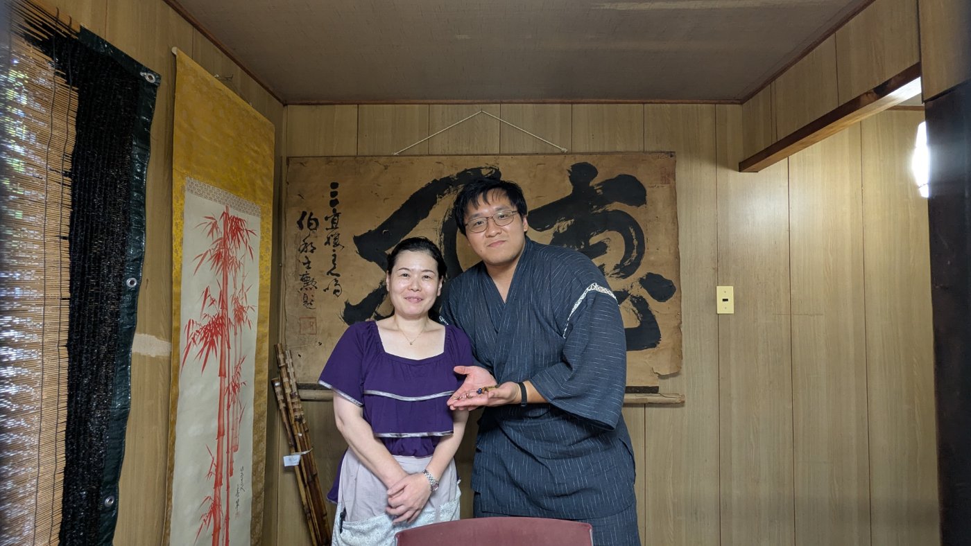 Skyler in yukata with a woman artisan before a bamboo scroll