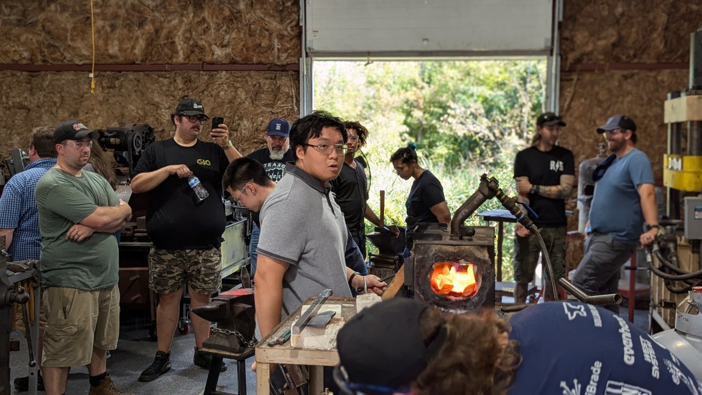 A blacksmithing class gathered around the forge and power hammer