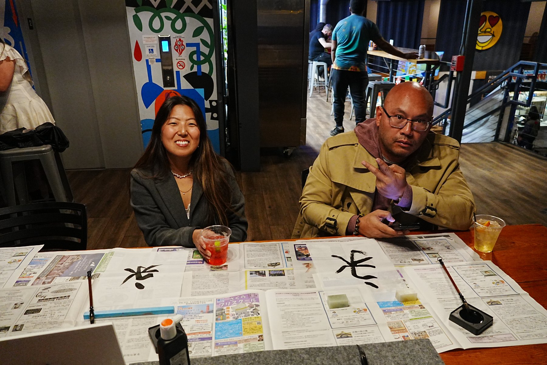 Two guests seated with their brushed characters spread across the table