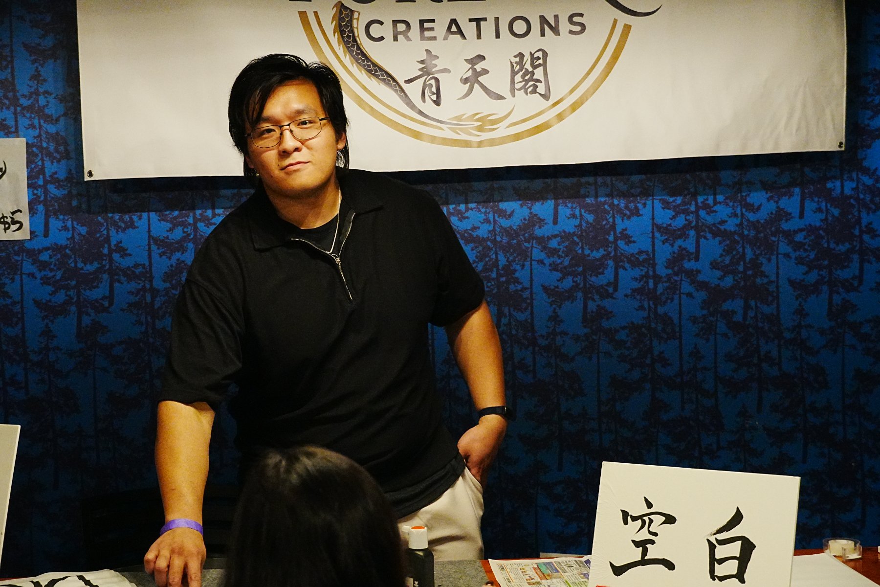 Skyler standing at the booth before the 青天閣 banner, a 空白 board in the foreground