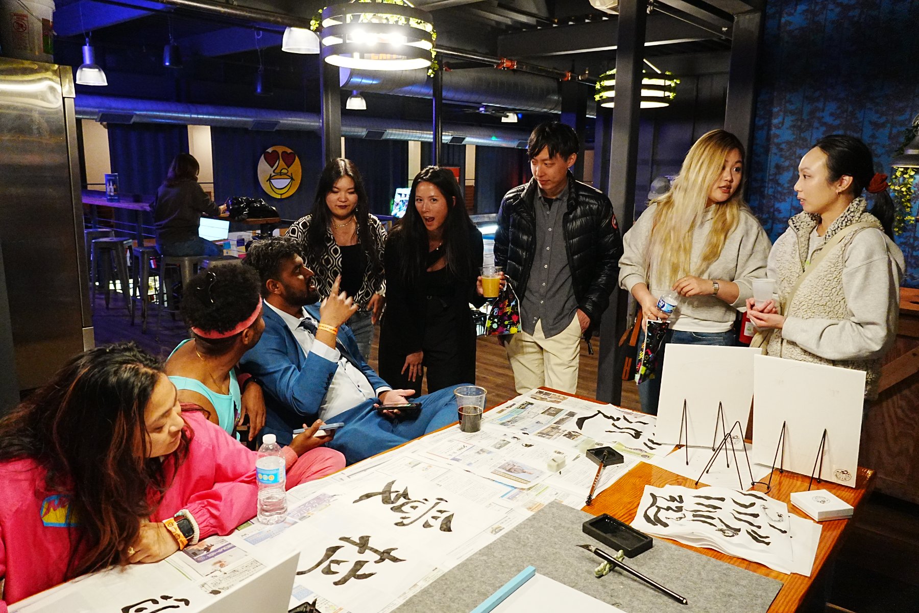 A group of guests gathered around the table, brushing characters on paper laid over newspaper