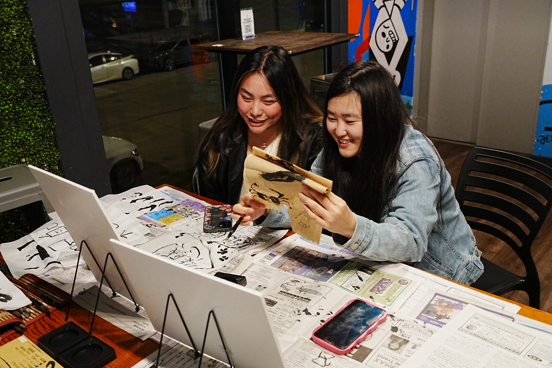 Two guests laughing over an ink painting of a crab on brown paper