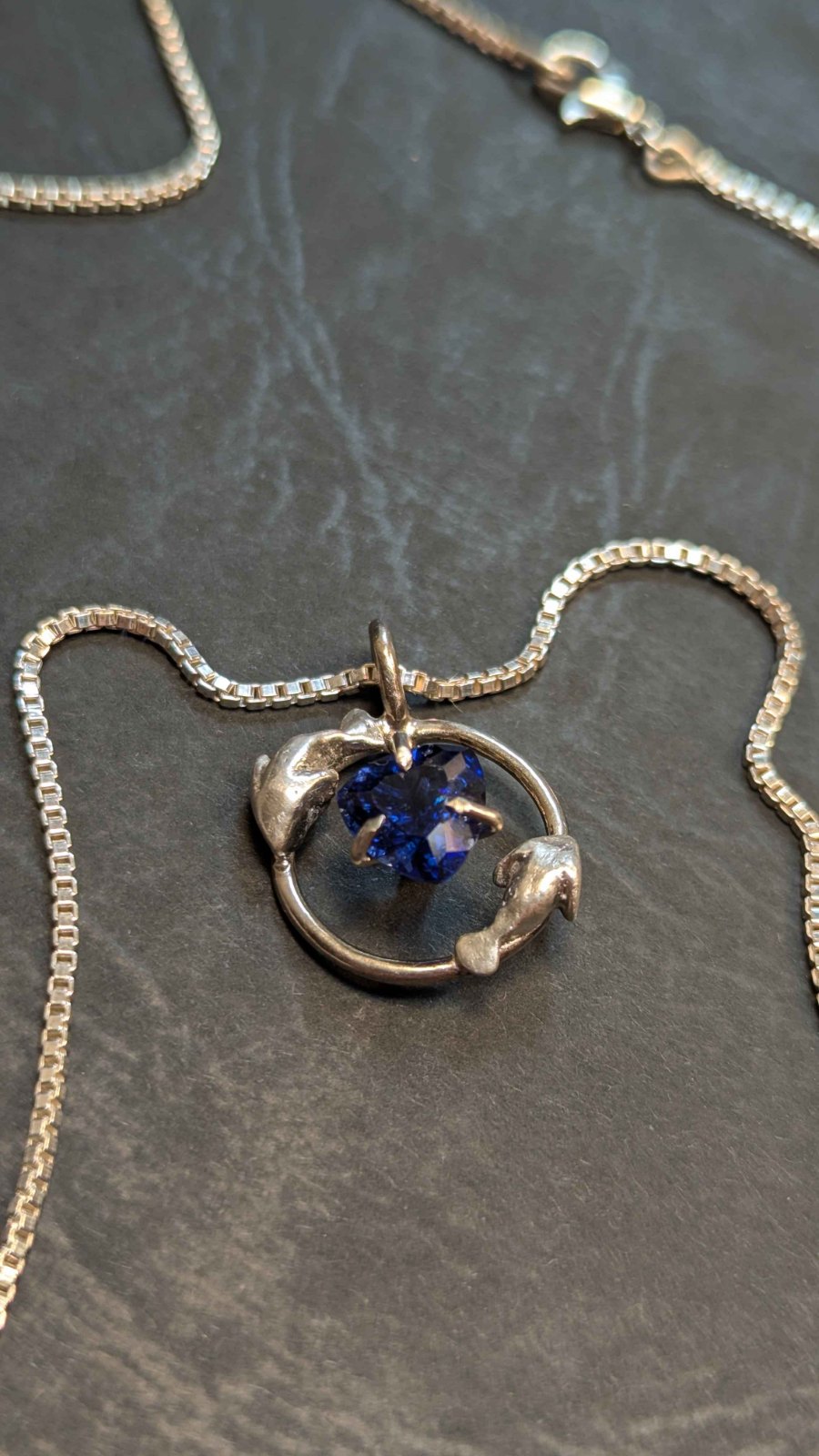 Azure Souls: two silver dolphins encircling a faceted blue heart gem on a box chain