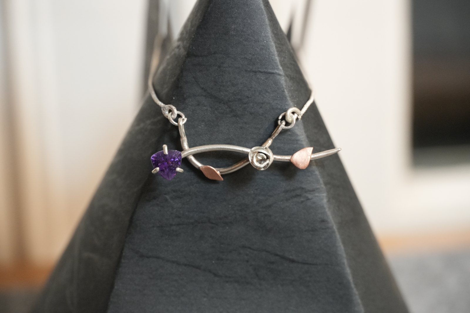 La Vie en Améthyste, front view: prong-set trillion amethyst at the end of a crossing silver vine with a silver rosebud and two copper leaves, on a box chain