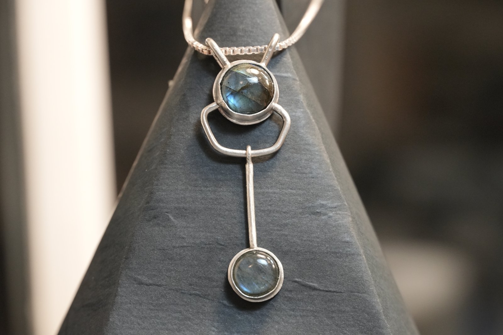 Midnight Sextant, front view: round labradorite cabochon with two raised loops, linked by a silver frame and bar to a second labradorite drop, on a box chain