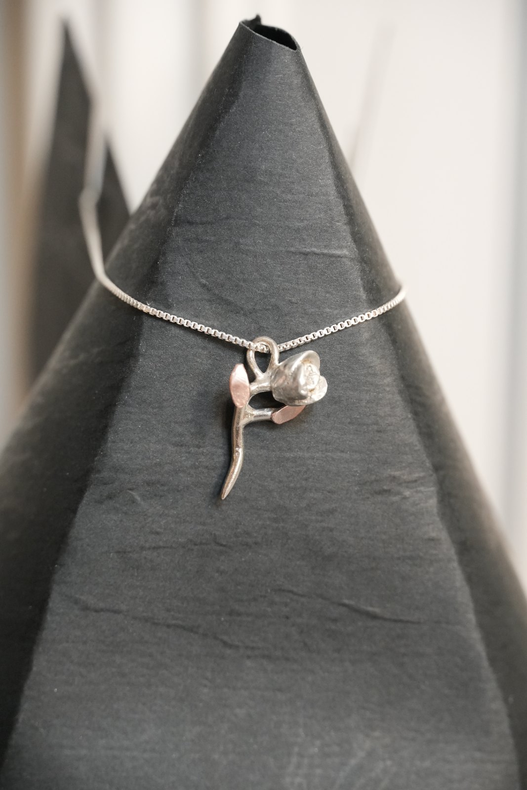 Silver Rose, front view: a small hand-formed silver rosebud on a curving silver stem with two copper leaves, on a box chain