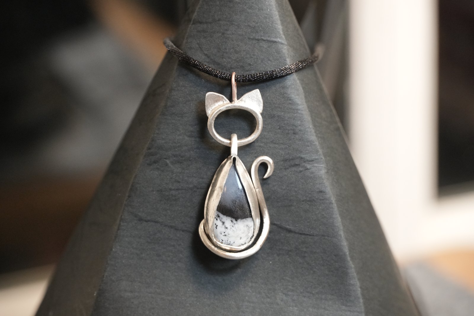 Teardrop Kitten in dendritic opal, front view: silver cat with pointed ears and curled tail framing a black-and-white dendritic teardrop, on a black cord