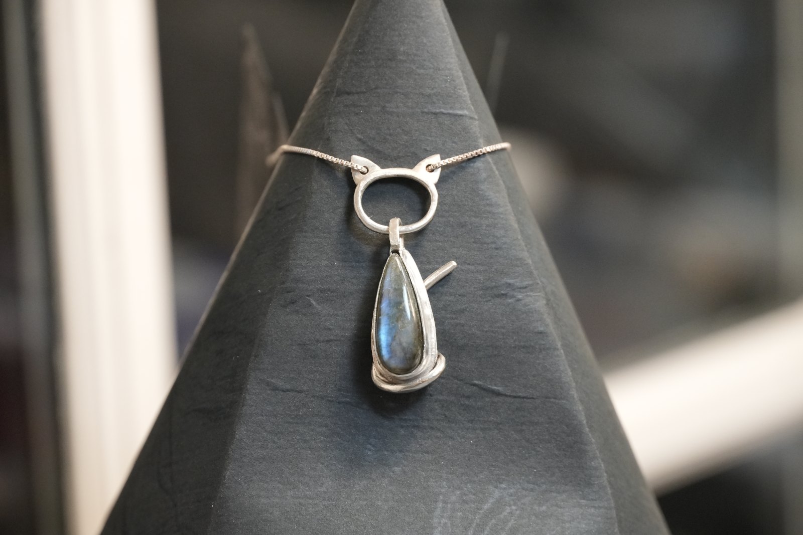 Teardrop Kitten in labradorite, front view: silver cat with the chain threaded through its ears, framing a blue-flash labradorite teardrop