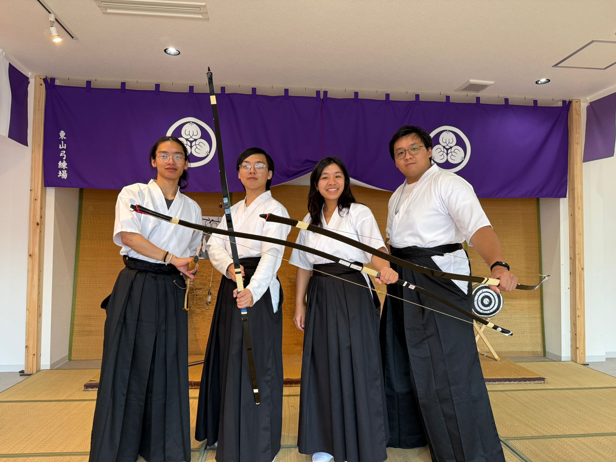 Kyudo group in white keikogi and black hakama holding longbows before a purple banner