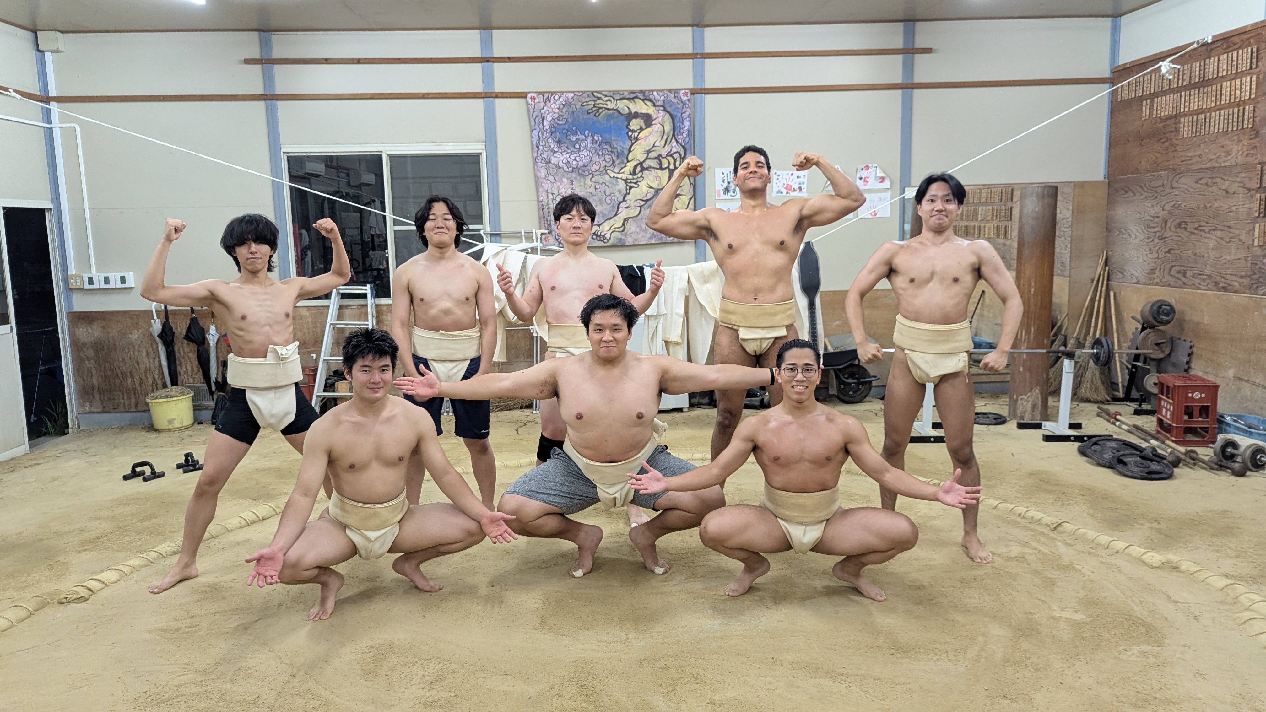 Sumo training group flexing in mawashi inside a sand keiko ring