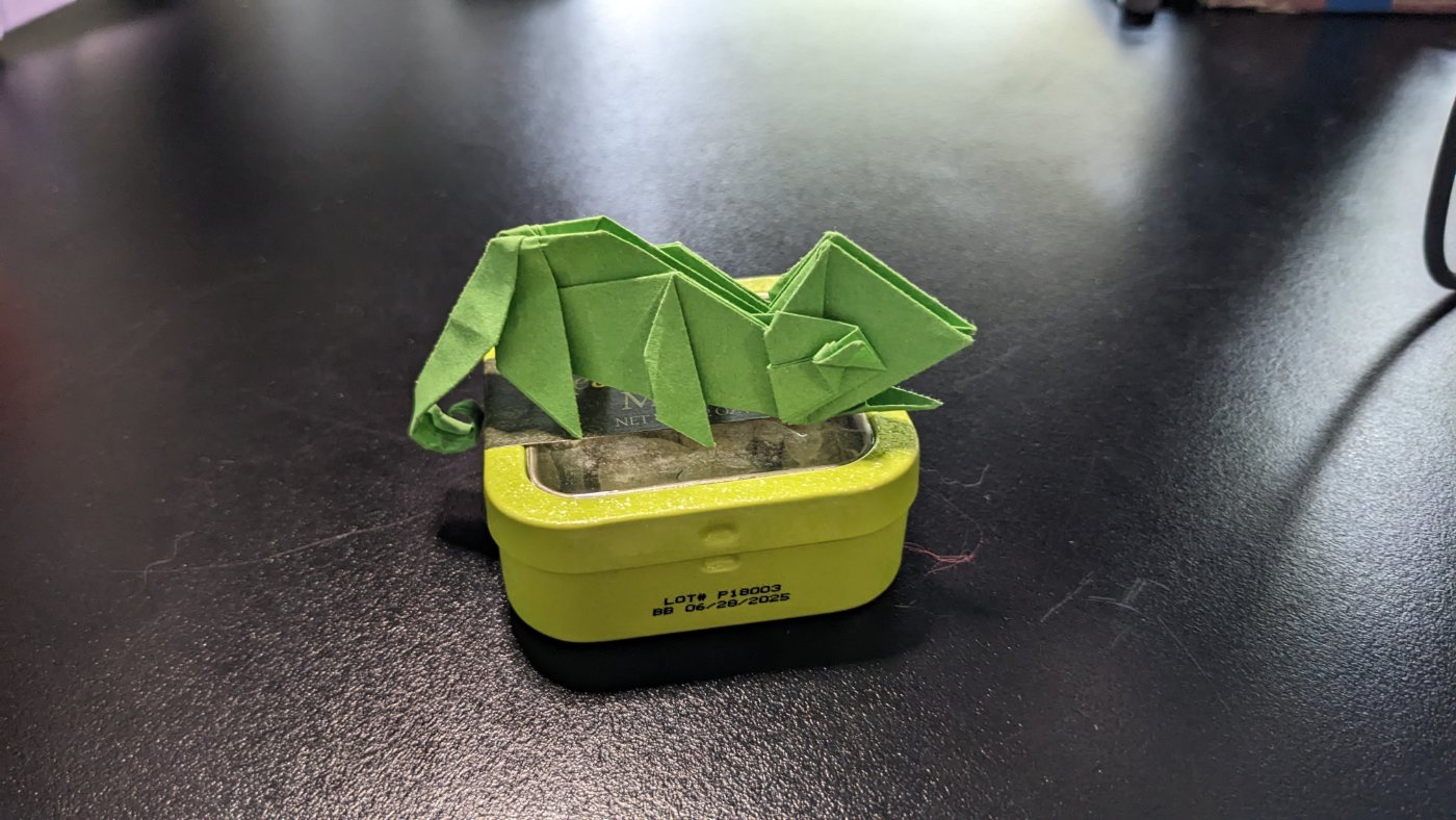 Green origami dragon perched on a tin