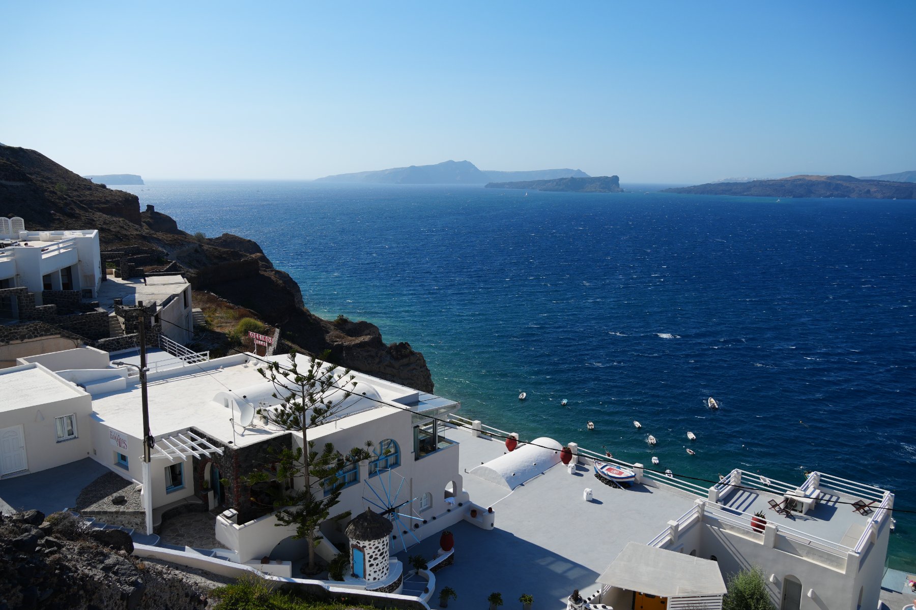 White cliffside villas above a deep blue caldera dotted with small boats, Santorini