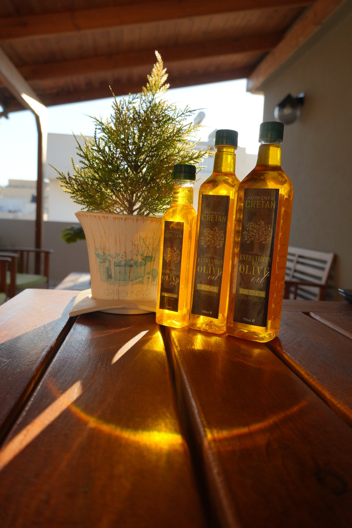 Three bottles of Authentic Cretan extra virgin olive oil glowing gold in backlight on a wooden table