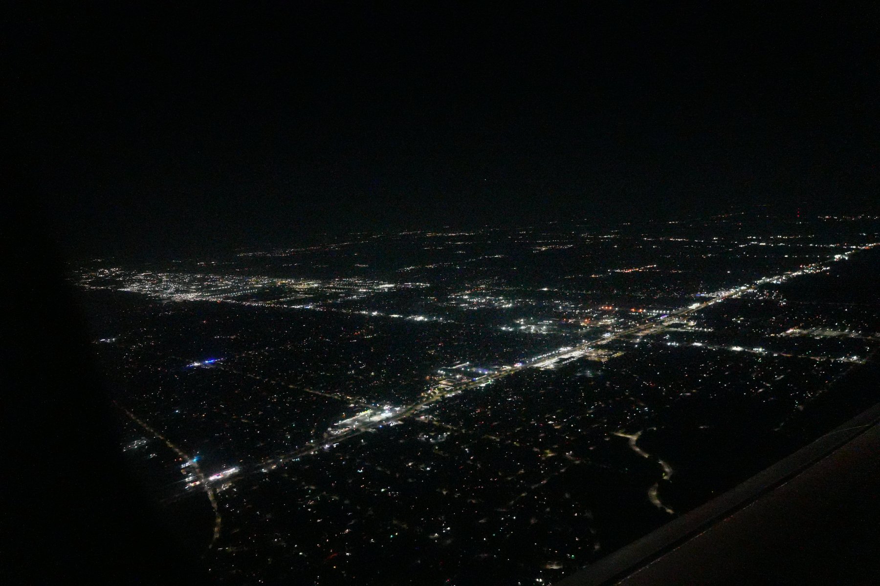 City lights spreading across the dark ground seen from an airplane window at night
