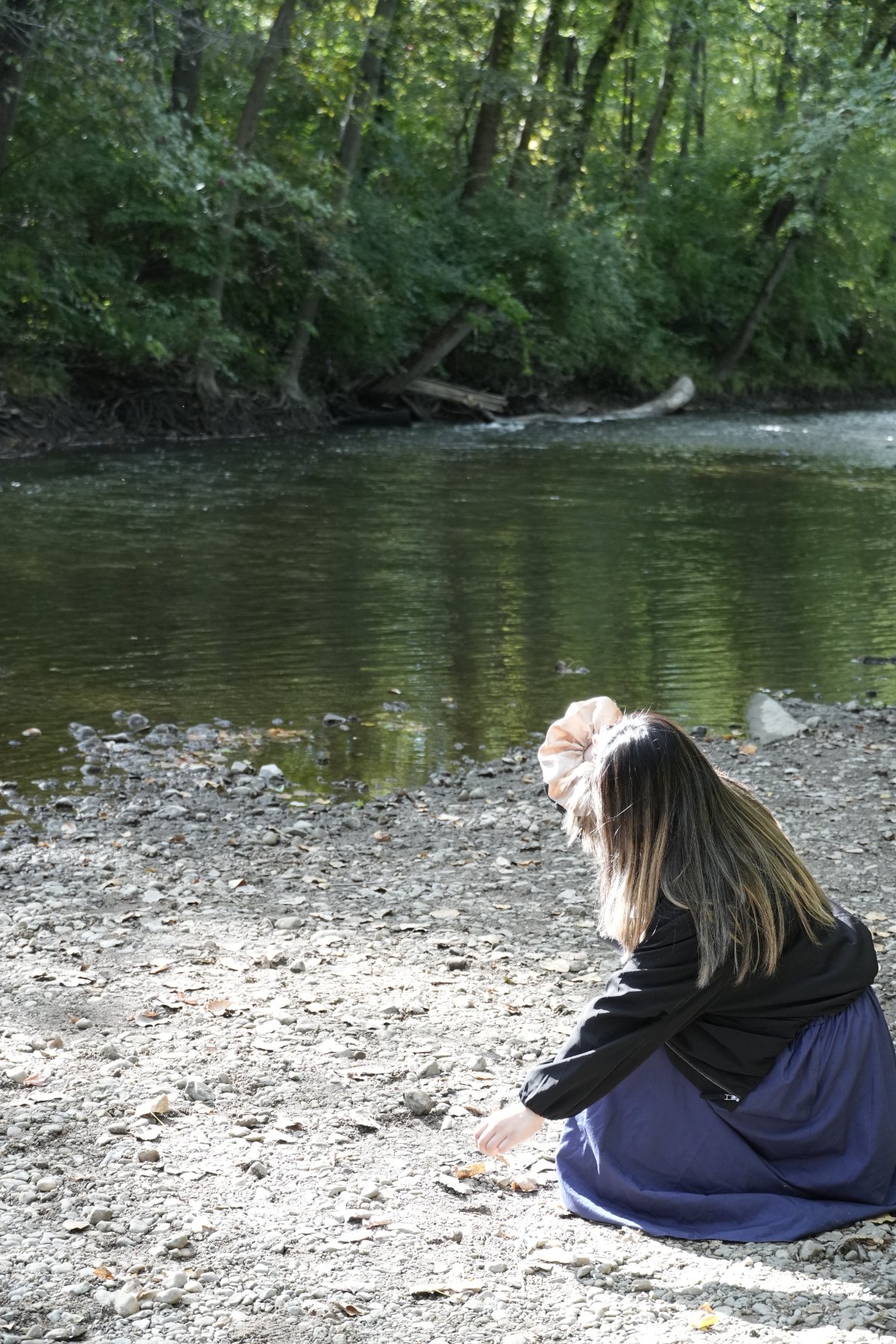 A woman seen from behind, kneeling at the water's edge with a large scrunchie in her hair