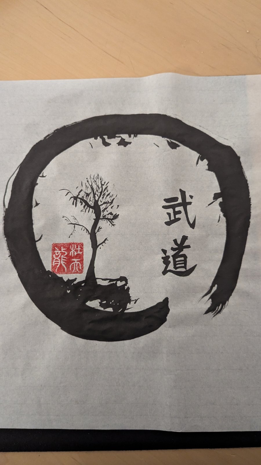 Ensō circle enclosing a bare ink tree on rock with the characters 武道 and a red seal