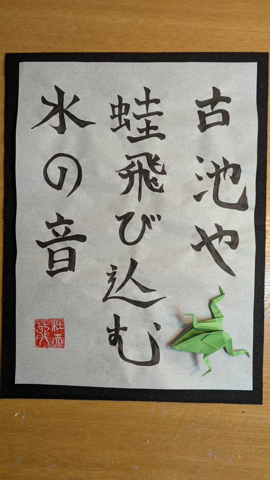 Shodo of Bashō's haiku 古池や蛙飛び込む水の音 beside a green origami frog