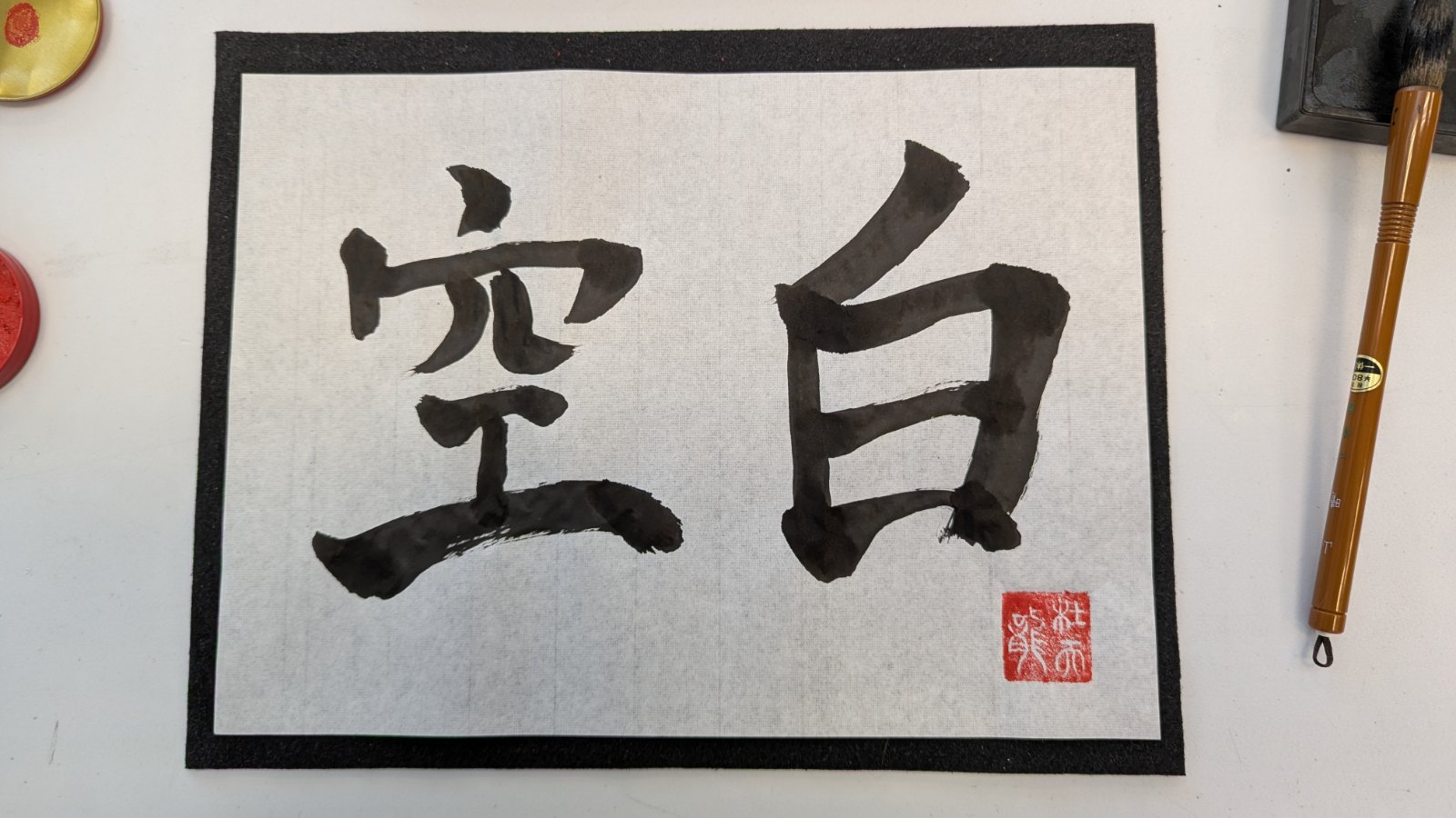 Shodo calligraphy of the two kanji 空白 (kūhaku, blank space) in black ink with a red seal